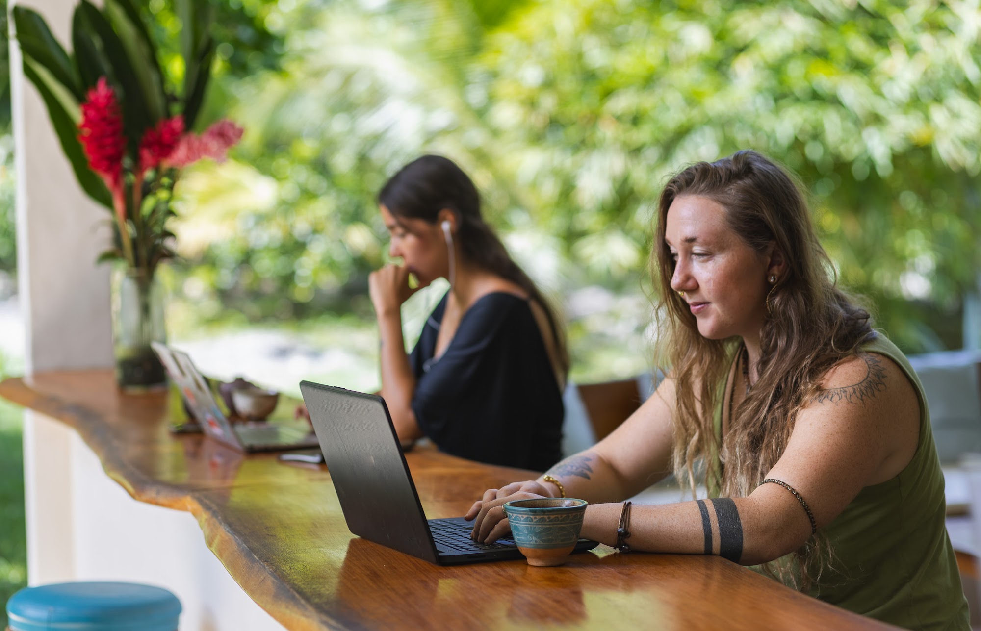 Two residents working on laptops at an open-air wooden counter facing the jungle